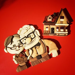 Puede incluir: Obra de arte en madera que representa a los personajes de la película "Up", junto a una casa. Los personajes están hechos de varias tonalidades de madera, con detalles negros. La casa, también de madera, tiene un tejado marrón y paredes beige, sobre fondo rojo.