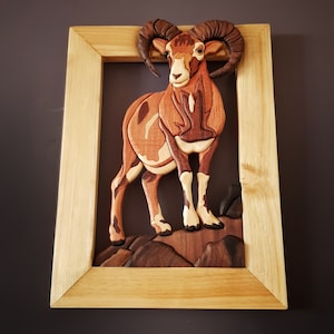 Puede incluir: Una escultura de pared de madera de un carnero marr&oacute;n y blanco con grandes cuernos rizados. El carnero est&aacute; de pie sobre una base de madera con un patr&oacute;n de veta de madera marr&oacute;n y gris.