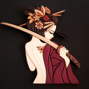 Puede incluir: Una escultura de madera de una mujer con una espada samurái. La mujer lleva un kimono rojo y tiene una flor en el pelo. La escultura está tallada y pintada de forma intrincada.