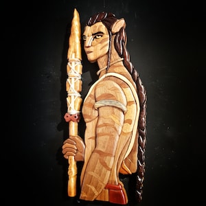 May include: A wooden sculpture of a humanoid figure with a long braid, holding a spear with white wrappings. The figure is carved with intricate details and has a striped pattern on its body.