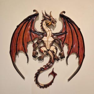 May include: A wooden dragon wall art piece. The dragon has a cream-colored chest and belly, with brown and reddish-brown wings and body. The wings are spread wide, and the dragon's tail curves gracefully. The artwork is mounted on a neutral-colored wall.