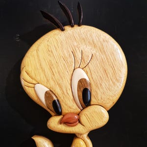 Puede incluir: Una talla de madera de Piol&iacute;n, un canario amarillo con ojos negros, un pico marr&oacute;n y una cresta marr&oacute;n. La talla es detallada y realista, con la veta de la madera visible.