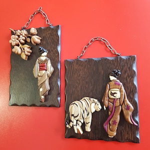 May include: Two wooden wall plaques with intricate carvings. The left plaque features a woman in a traditional Japanese kimono with a floral design. The right plaque features a woman in a similar kimono with a tiger beside her.