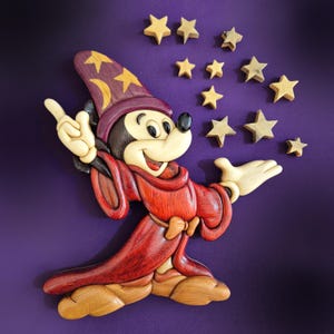 May include: Wooden wall art featuring Mickey Mouse as a sorcerer, wearing a red robe and a purple hat with yellow stars. The artwork includes several wooden stars floating in the air, all set against a purple background.