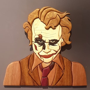 Könnte beinhalten: Eine Holzskulptur des Jokers aus den Batman-Comics. Die Skulptur ist aufwendig geschnitzt und bemalt, mit einer detaillierten Darstellung des Gesichts und der Haare des Jokers. Der Joker trägt einen braunen Anzug mit einer roten Krawatte.