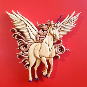 May include: A wooden sculpture of a unicorn with wings. The unicorn is carved in a light wood and has a pink horn. The wings are spread out and are also carved in wood.