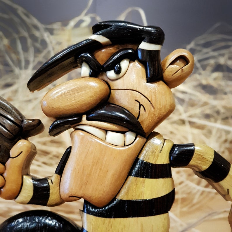 May include: A wooden cartoon character with a black and yellow striped shirt, a black hat, and a large, exaggerated nose. The character has a mischievous expression with a wide grin and a raised eyebrow.