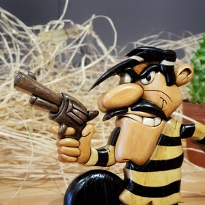 May include: A wooden figurine of a cartoon character with a black and yellow striped shirt, holding a brown wooden gun. The character has a large nose, a black mustache, and a scowling expression.