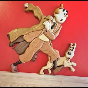 Może przedstawiać: Drewniana rzeźba przedstawiająca mężczyznę biegnącego z psem. Mężczyzna ma na sobie brązowy płaszcz i ma zaskoczony wyraz twarzy. Pies jest brązowo-biały i biegnie za mężczyzną.