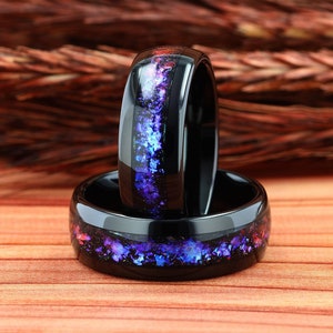 Pu&ograve; includere: Due anelli in ceramica nera con un'incisione di glitter viola e blu. Gli anelli sono impilati uno sopra l'altro.