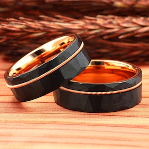 Puede incluir: Dos anillos de carburo de tungsteno negro con una incrustaci&oacute;n de oro rosa. Los anillos tienen un acabado martillado y una fina banda de oro rosa alrededor del centro.