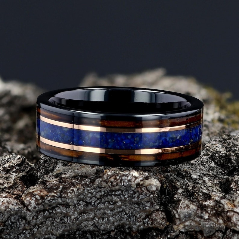 May include: A black ceramic ring with a copper and lapis lazuli inlay. The ring is set on a piece of rough bark.