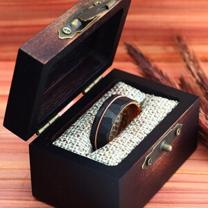 Puede incluir: Un anillo de carburo de tungsteno negro y oro rosa con acabado martillado, presentado en una caja de anillo de madera con forro de terciopelo marr&oacute;n.