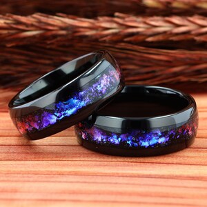 Pu&ograve; includere: Due anelli in ceramica nera con un design a forma di galassia con accenti viola, blu e rosso. Gli anelli sono impilati uno sopra l'altro.