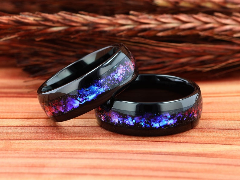 Pu&ograve; includere: Due anelli in ceramica nera con un design a forma di galassia con accenti viola, blu e rosso. Gli anelli sono impilati uno sopra l'altro.