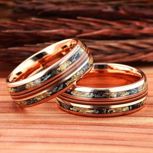 May include: Two rose gold wedding bands with a copper wire inlay and black and gold flecks.