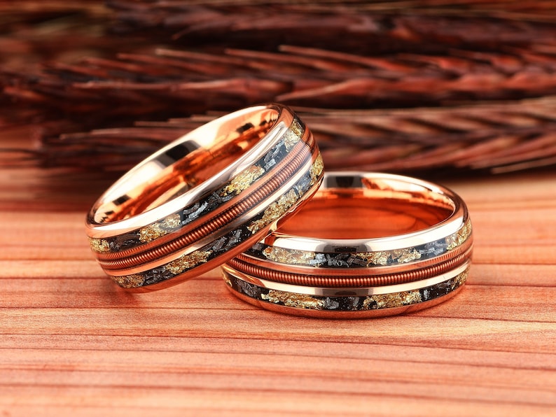 May include: Two rose gold wedding bands with a copper wire inlay and black and gold flecks.
