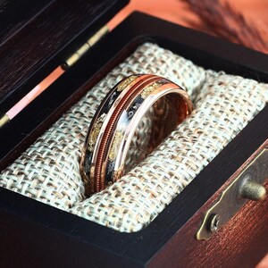 May include: A gold and copper ring with black and gold inlay in a wooden ring box with a brown velvet lining.