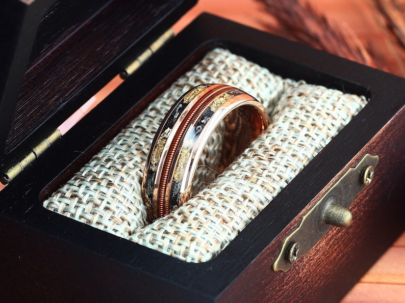 May include: A gold and copper ring with black and gold inlay in a wooden ring box with a brown velvet lining.