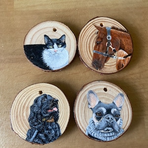May include: Four wooden ornaments featuring hand-painted pet portraits. Includes a black and white cat, a brown horse with a bridle, a black dog, and a grey and black dog wearing a grey scarf. Each has a hole for hanging.