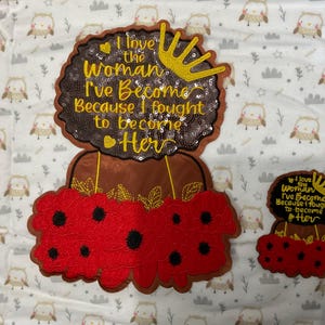 May include: Two embroidered patches. The larger patch features a brown afro with a gold crown, red poppies, and the text "I love the Woman I've Become Because I fought to become Her." A smaller matching patch is also present.