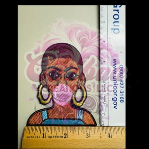 May include: An embroidered patch of a woman with brown skin, wearing a blue tank top and large gold hoop earrings. She is blowing a pink bubble. The patch is about 2 inches tall.