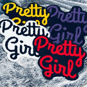 Könnte beinhalten: Vier handgefertigte Teppiche mit den Worten "Pretty Girl" in Schreibschrift. Die Teppiche sind in Schwarz, Weiß und Schwarz mit gelben, lila und roten Buchstaben. Die Teppiche liegen auf einer grauen, flauschigen Oberfläche.