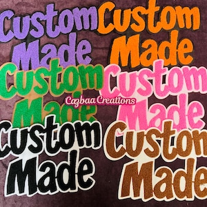 May include: A collection of "Custom Made" patches in various colors, including purple, orange, green, pink, black, and brown. Each patch features a unique color combination with a textured, glittery appearance. The patches are arranged on a dark purple background.