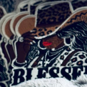 May include: Embroidered patches featuring a woman wearing a cowboy hat with a leopard print design. The woman has dark skin, red lipstick, and the word "BLESSED" is embroidered below the image.