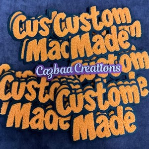 May include: A collection of orange and black custom-made patches with a fuzzy texture. The text "Custom Made" is repeated multiple times in a bold, stylized font. A smaller purple and white label reads "Cazbaa Creations".