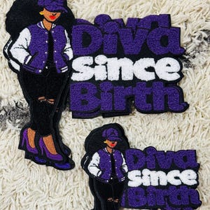 May include: Embroidered patches featuring a woman in a purple and white jacket, black pants, and purple heels. The patches have the text "Diva Since Birth" in purple and white.