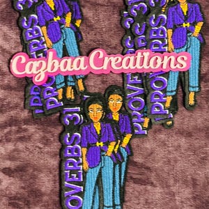 Könnte beinhalten: Gestickte Aufnäher mit einer Frau in einem lila Blazer, blauen Jeans und schwarzen Schuhen. Die Aufnäher tragen den Text "PROVERBS 31" und "Cazbaa Creations" in Pink. Die Aufnäher befinden sich auf einem weinroten Hintergrund.