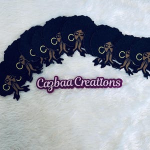 May include: A set of eight black felt patches featuring a stylized image of a woman with her hands clasped in prayer. Each patch has a gold circle with the letter "C" inside. The patches are arranged in a semi-circle with the text "Cazbaa Creations" in purple below.