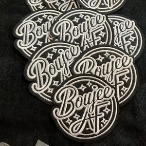 May include: A collection of black and white embroidered patches. Each patch is circular with the word "Boujee AF" in a stylized script font. The design includes stars and a decorative border.