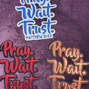 May include: Three embroidered patches with the words "Pray, Wait, Trust" and the reference "Matthew 21:22". One patch is blue, one is red, and one is orange. The patches have a sequined appearance.