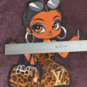 May include: An embroidered patch depicting a cartoon woman with sunglasses, hoop earrings, and a leopard print dress. She is holding a phone and a purse. The patch is approximately 20 cm in length.