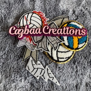 May include: A selection of volleyball-themed patches and embellishments. The design includes a volleyball, a lightning bolt, and the text "Cazbaa Creations" in pink. The patches feature white, gold, blue, and red accents, with a glittery silver bow.