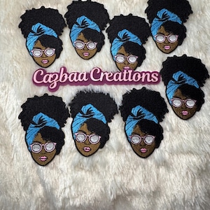 May include: Embroidered patches featuring a Black woman with glasses and a blue head wrap. The patches have black curly hair and pink lips. The text "Cazbaa Creations" is in pink and purple.