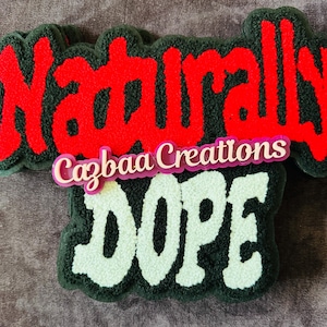 Puede incluir: Primer plano de un parche decorativo con las palabras "Naturally DOPE" en rojo y blanco, con un borde verde y negro. También es visible el texto "Cazbaa Creations".