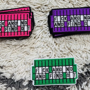 Puede incluir: Tres parches bordados rectangulares con un diseño de cuadrícula y el texto FUCK AROUND AND FIND OUT. Un parche es rosa brillante, otro es morado y otro es verde. Cada parche tiene un borde negro y letras blancas sobre un fondo de cuadrícula.