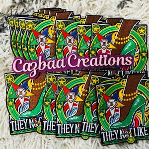 May include: A stack of embroidered patches featuring a green high-heeled shoe with a brown leg, gold jewelry, and a star design. The patches have the text "THEY N' LIKE" and "Cazbaa Creations".