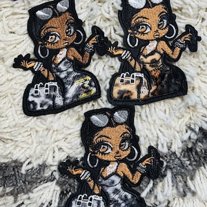 Puede incluir: Tres parches bordados que muestran un personaje estilizado de piel oscura, con gafas de sol en la cabeza, pendientes de aro y pulseras. El personaje sostiene un objeto pequeño y un bolso, con el texto cazbaacreations visible arriba.