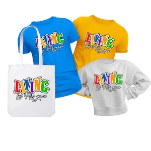 May include: A collection of apparel including a blue t-shirt, yellow t-shirt, and gray sweatshirt, along with a white tote bag. Each item features the text "LIVING by His grace" in a colorful, outlined font.