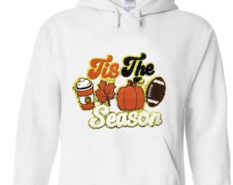 May include: White hoodie featuring a seasonal design. The graphic includes a coffee cup, a maple leaf, a pumpkin, and a football, with the text "Tis The Season" in orange, black, and gold.