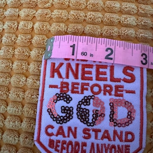 Puede incluir: Parche bordado con el texto "KNEELS BEFORE GOD CAN STAND BEFORE ANYONE" en hilo rojo. El parche mide aproximadamente 6,35 cm de ancho y 7,62 cm de alto. Las letras "GOD" están adornadas con lentejuelas.