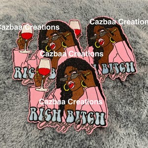May include: Embroidered patches featuring a woman in a pink blazer, sunglasses, and gold hoop earrings, holding a wine glass. The patches have the text "RICH BITCH Energy Only" in a stylized font. The brand name "Cazbaa Creations" is also visible.
