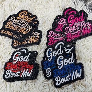 May include: Embroidered patches in various colors, including gold, pink, red, and blue. Each patch features the phrase "God Don't Play Bout Me!" in a stylized font. The patches have a black border and are likely for clothing or accessories.