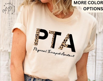 Op de afbeelding: Een crèmekleurig T-shirt met de tekst "PTA" in zwarte letters op een luipaardprint achtergrond. De tekst "Physical Therapist Assistant" staat in zwarte cursieve letters onder de letters.