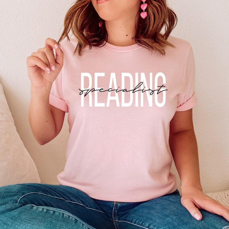 Puede incluir: Una camiseta rosa con el texto "READING specialist" en letras blancas.