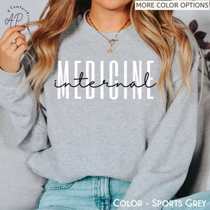 May include: A gray sweatshirt with the text "internal medicine" printed in white on the front. The sweatshirt is being worn by a person with long blonde hair. The text "COLOR - SPORTS GREY" is printed at the bottom of the image.
